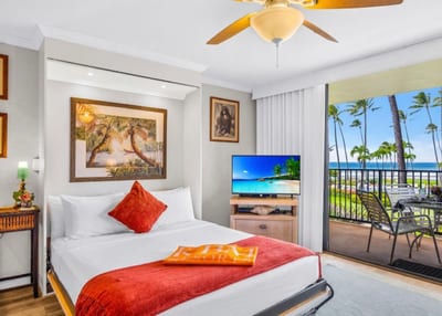 The primary bedroom features warm tropical artwork near the ocean-facing sliding doors