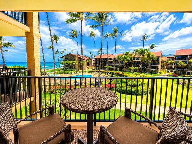 Balcony seating for two sits just off the main living space, with palms and the Pacific ahead