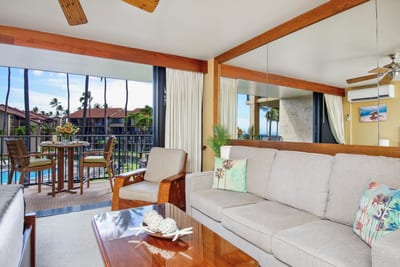 Relax beneath cooling fans in a bright, mirror-kissed living room where hand-carved chairs add a touch of aloha flair