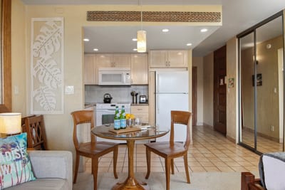 Enjoy cozy island meals at this glass-top dining table set for two, surrounded by warm wood tones and tropical charm