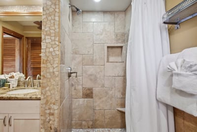 Step into the tiled walk-in shower, framed by natural stone accents and soft lighting, perfect for a quiet daily escape