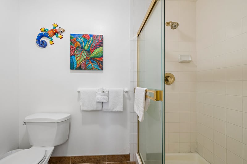 This bright guest bath features a large vanity, charming island artwork, and a clean glass-enclosed shower for comfort