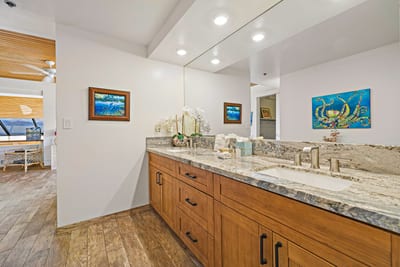 This guest bath invites calm with its granite double vanity, warm wood cabinetry, and expansive mirrored lighting