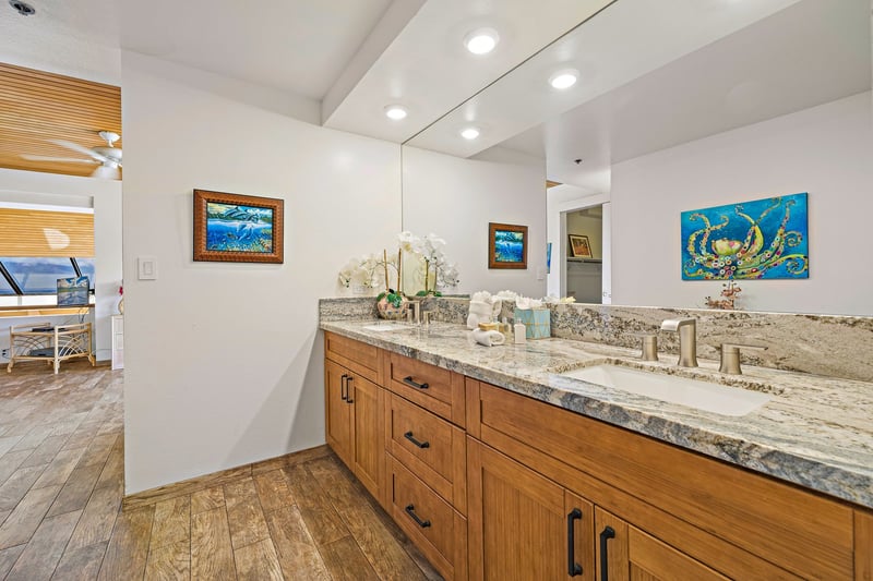 This guest bath invites calm with its granite double vanity, warm wood cabinetry, and expansive mirrored lighting
