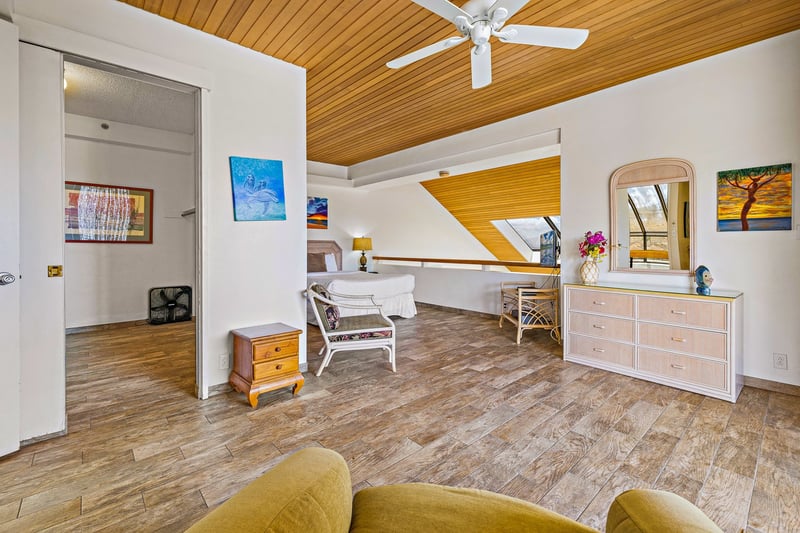 This open-concept master suite features a luxe bed, golden wood ceilings, and glass doors to a view-filled balcony