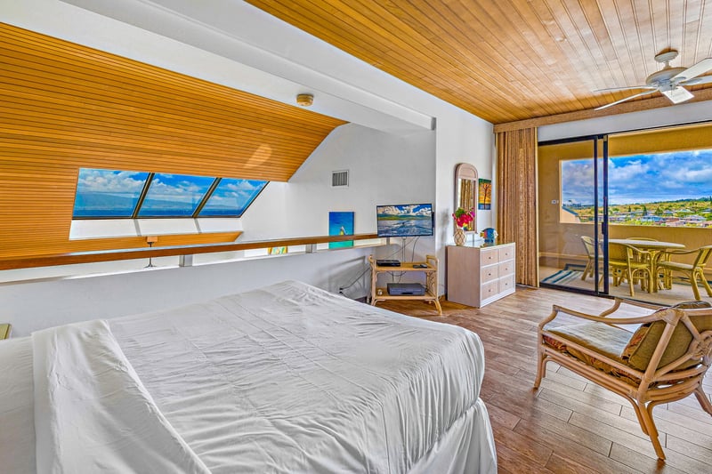 The vaulted-ceiling master bedroom pairs crisp bedding and coastal art with panoramic views of sea, sky, and sand