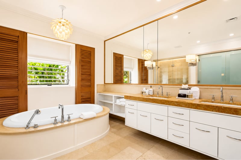 Primary bathroom at The Resort at Kapalua Bay MON-2206 — deep soaking tub beneath a shell pendant chandelier beside a dual vanity MON-2206