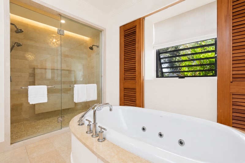 Primary bath at The Resort at Kapalua Bay MON-2206 — glass walk-in shower and soaking tub side by side beneath louvered shutters MON-2206