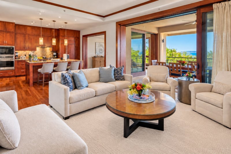 Open plan living room with deep sofas, swivel armchairs, and views to the kitchen and lanai
