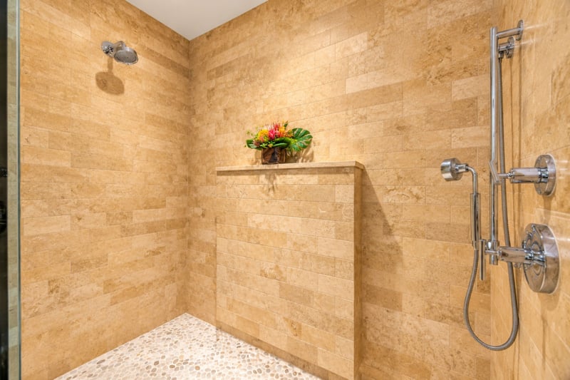 Primary bathroom walk in shower with stone tile, rain shower head, and handheld sprayer