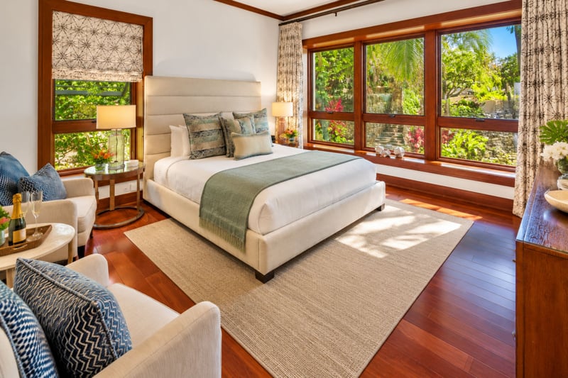 Second bedroom with upholstered bed, cozy seating, and garden views through corner windows