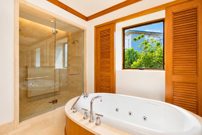 Primary bath at The Resort at Kapalua Bay MON-6301 — deep soaking tub beneath a garden-view window beside the walk-in shower