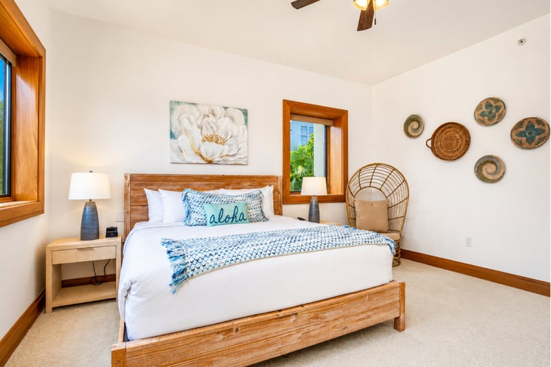 Guest bedroom at The Resort at Kapalua Bay MON-6301 — king bed, woven wall art, and a rattan accent chair