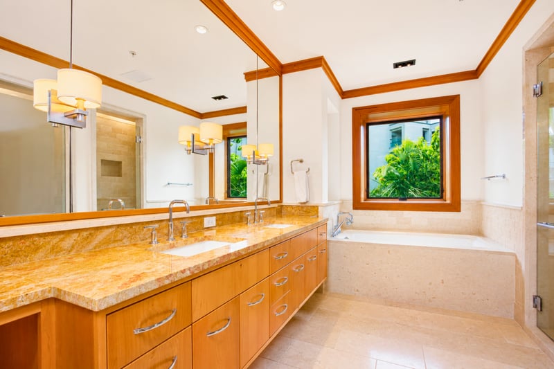 Guest bathroom at The Resort at Kapalua Bay MON-6301 — dual-sink granite vanity and soaking tub beneath a garden-view window