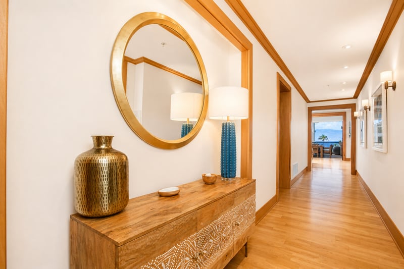 Entry hallway at The Resort at Kapalua Bay MON-6301 — console table, round brass mirror, and hardwood flooring leading to the living areas