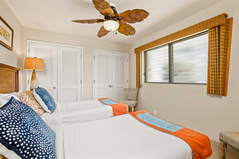 Crisp white twin beds with tropical wood frames and vibrant throws offer both charm and comfort for guest relaxation