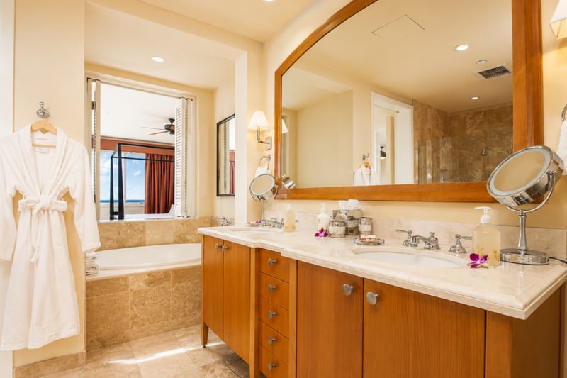 Primary bath vanity at Wailea Beach Villas PH505 — wood-framed mirror and plush robes with a glimpse of the ocean beyond WBV-PH505