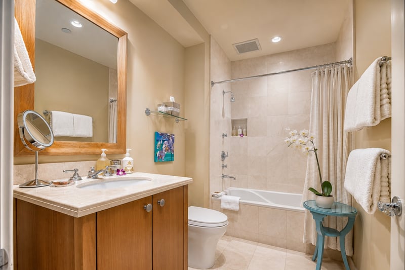 Guest bathroom vanity at Wailea Beach Villas PH505 — wood-framed mirror and tub-shower combo beyond WBV-PH505