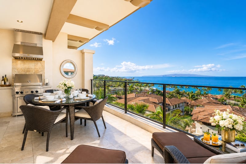 Oceanfront lanai at Wailea Beach Villas PH505 — private BBQ kitchen, dining for four, and panoramic Pacific views past the resort rooftops WBV-PH505