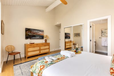 Primary bedroom at Kuilima Estates West W11 — king bed, ceiling-mounted TV, mirrored closet, and en-suite bathroom access