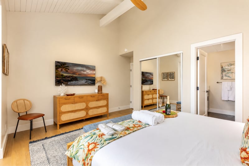 Primary bedroom at Kuilima Estates West W11 — king bed, ceiling-mounted TV, mirrored closet, and en-suite bathroom access KUL-W11