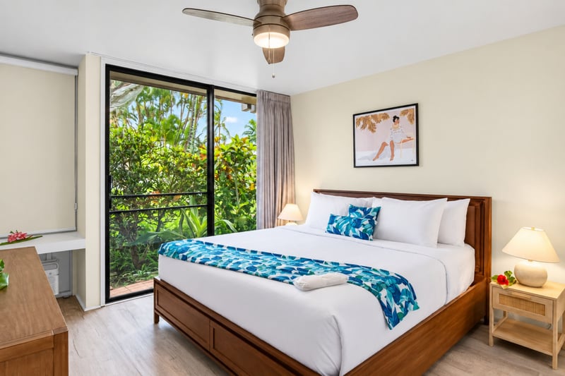 Primary bedroom at Kuilima West Estates 144, with a king bed, private lanai access, and lush tropical greenery just outside the door.