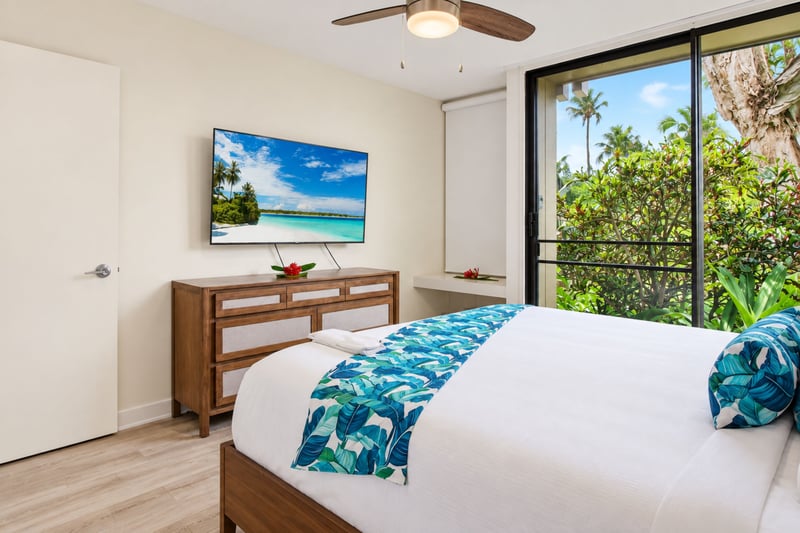 Primary bedroom at Kuilima West Estates 144, with a wall-mounted smart TV and a wood dresser facing the king bed.