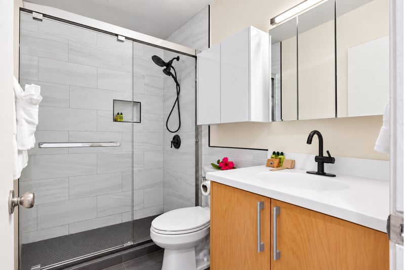 Primary bathroom at Kuilima West Estates 144, with a glass shower, matte black fixtures, and a dual-mirror vanity.