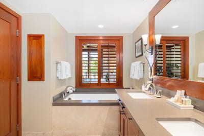 Spacious and sunlit, this guest bath welcomes with dual vanities, plush towels, and a hint of upscale island flair