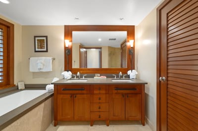 The mirror stretches wide like a portal to paradise, reflecting double sinks, glowing wood, and self-care rituals