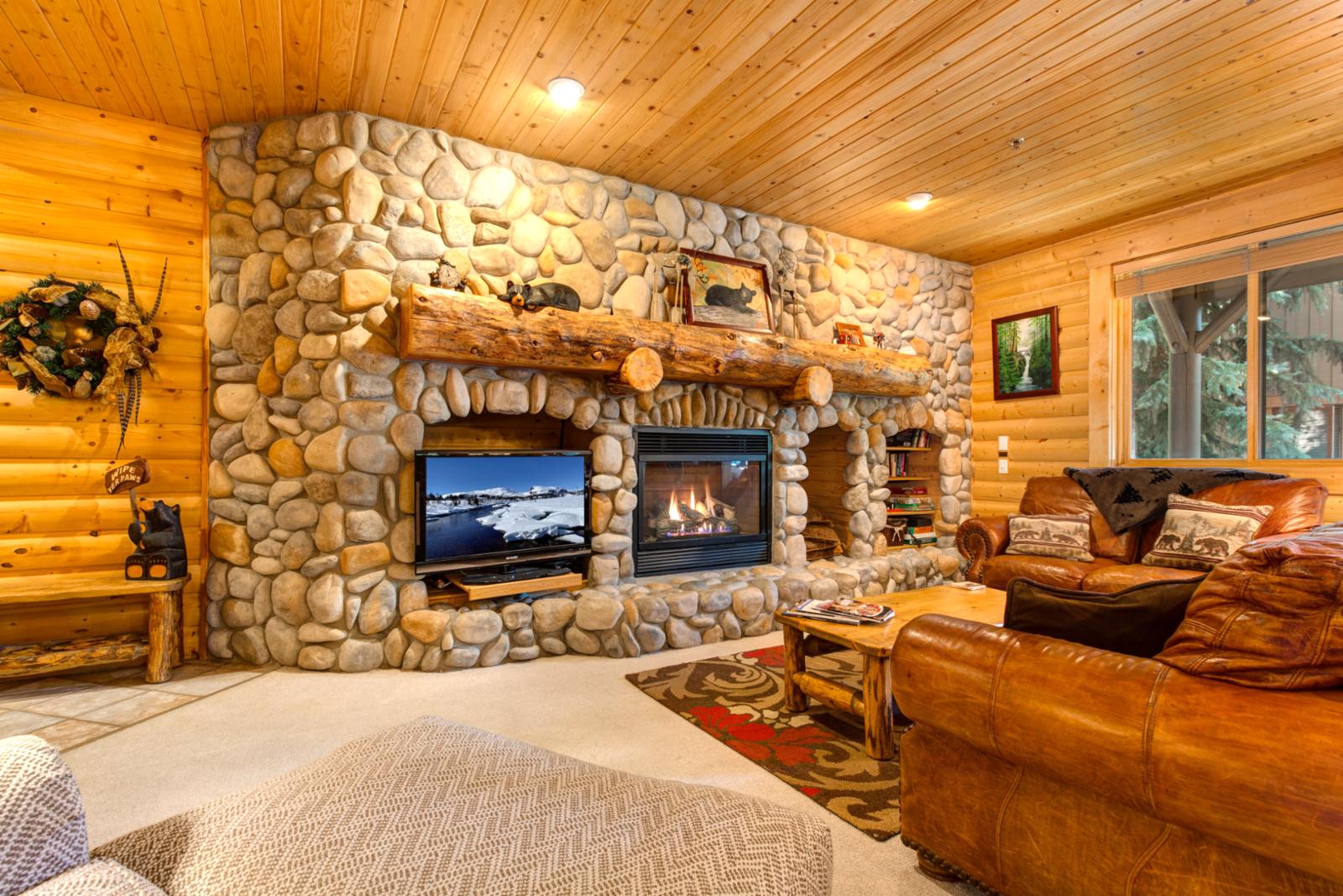 Gather in the cozy living room with a river rock fireplace, wood-paneled ceilings, and mountain lodge charm throughout.
