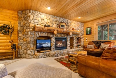 Gather in the cozy living room with a river rock fireplace, wood-paneled ceilings, and mountain lodge charm throughout.