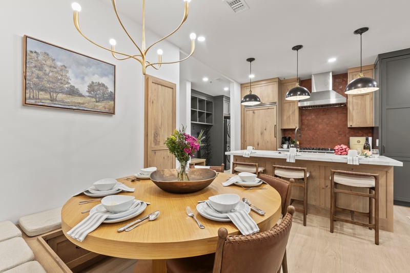A round dining table for four sits beneath a sculptural light fixture, with views into the modern kitchen.
