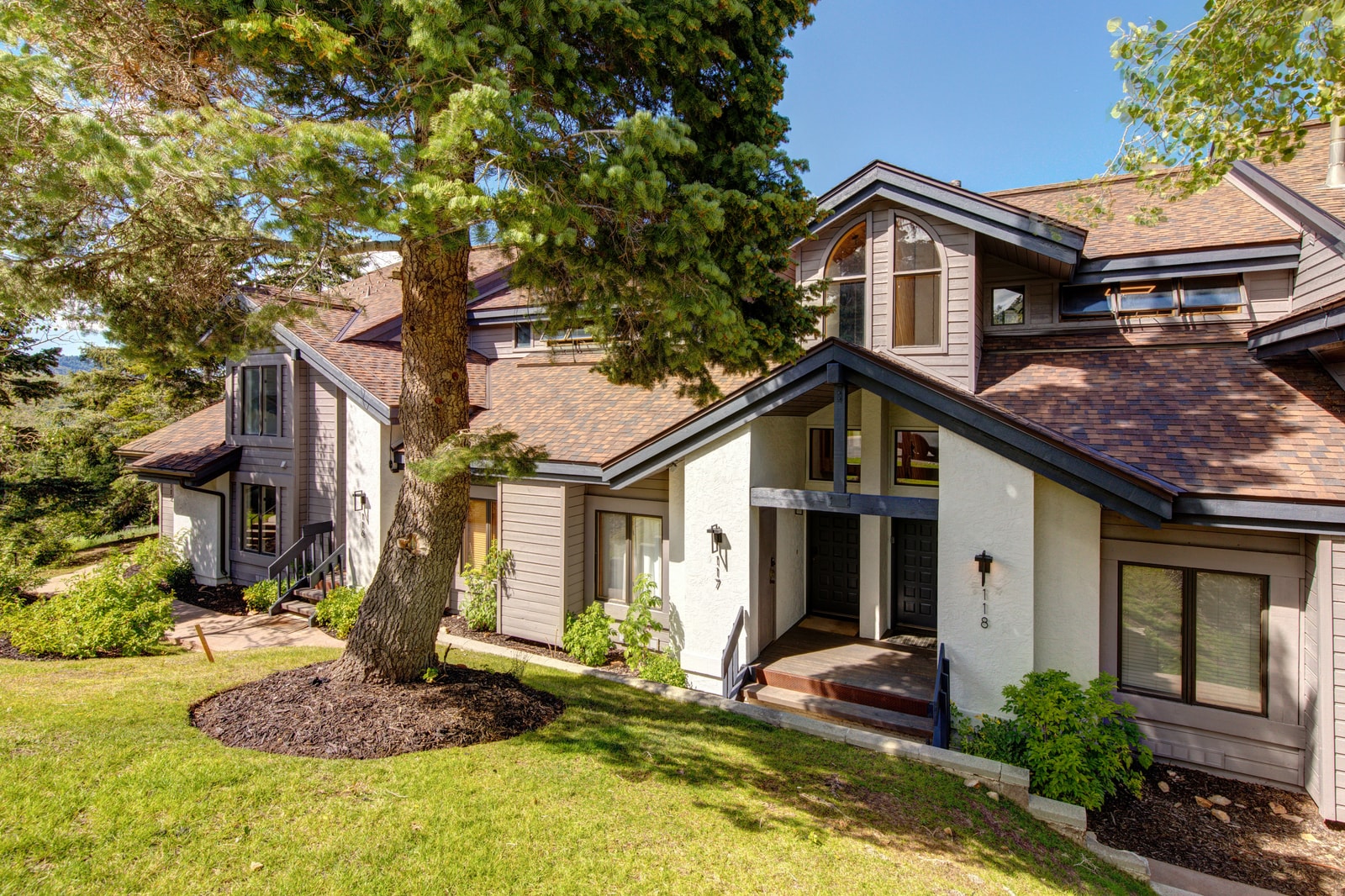 Charming summer exterior framed by tall trees and fresh landscaping.