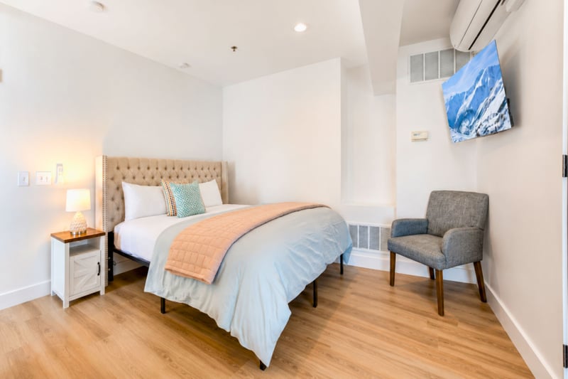 This bedroom features a tufted upholstered headboard, mounted smart TV, and its own air conditioning unit for year-round comfort.