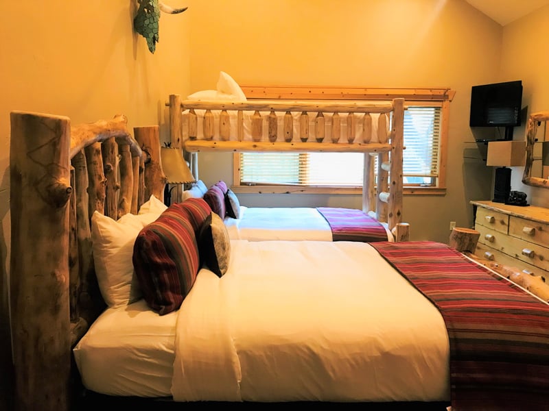 Cozy and spacious, this guest room includes multiple beds, mountain-themed art, and wood ceilings.