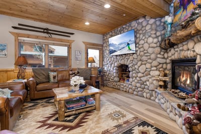 Warm living room: stone fireplace, rustic furniture, mountain views, cozy charm.