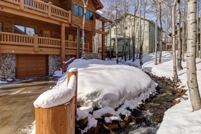 Snowy retreat with garage, beside stream and birch tree grove.