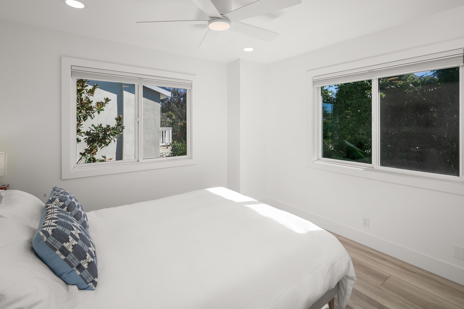Guest bedroom offers a bright, minimal setup with a comfortable bed and windows overlooking the surrounding greenery.