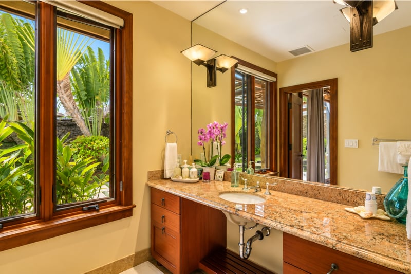 The ensuite guest bath features ample counter space and lush tropical foliage just outside the window