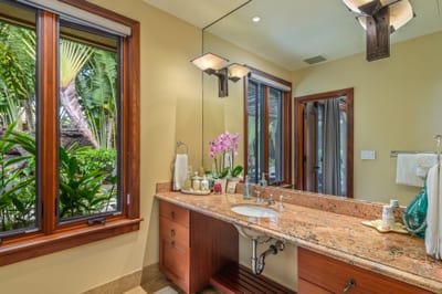 The ensuite guest bath features ample counter space and lush tropical foliage just outside the window