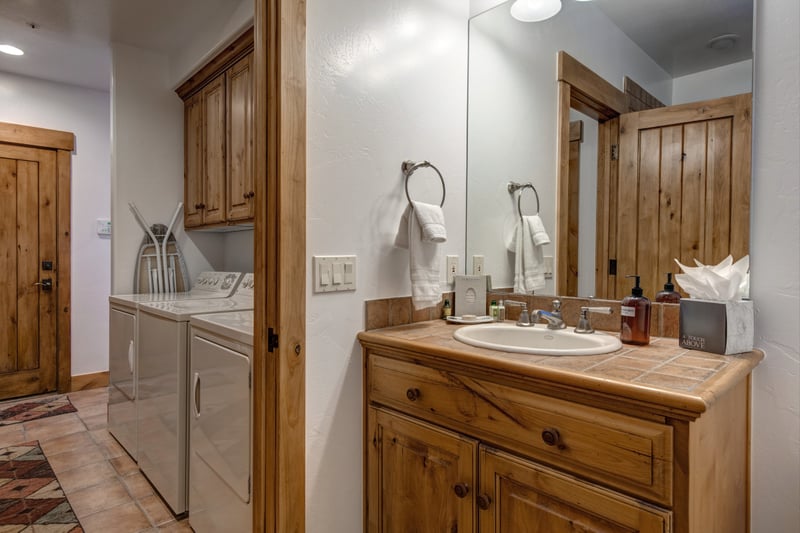 Laundry room and powder bath with full-size washer/dryer plus a tiled vanity sink for guest convenience