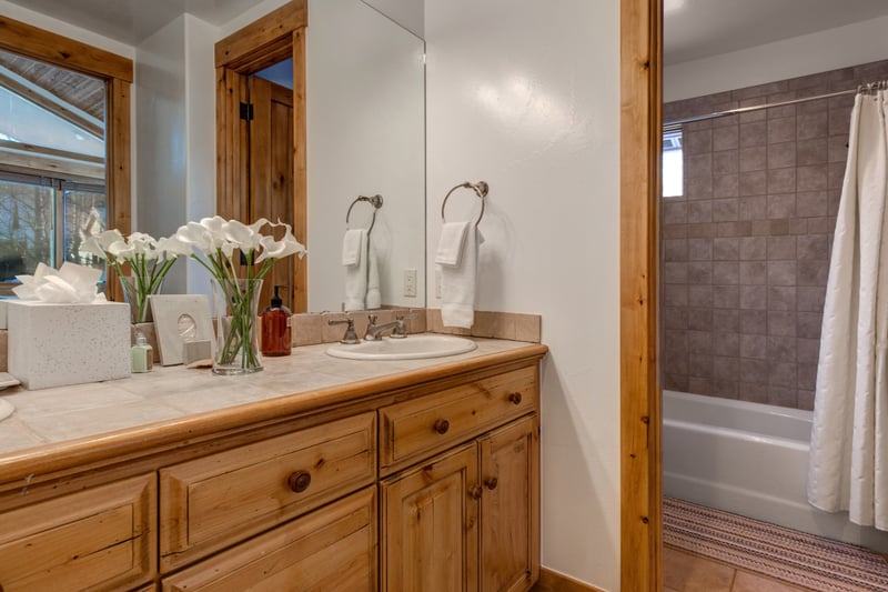 Guest bathroom with tub/shower combo with warm wood vanity and tile backsplash