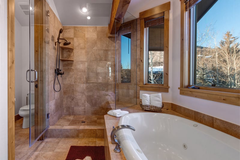 Primary bathroom with jetted soaking tub and glass walk-in shower framed by mountain-view windows