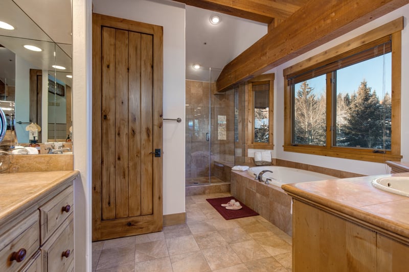 Primary suite ensuite at with dual vanities, glass shower, and jetted tub with mountain views