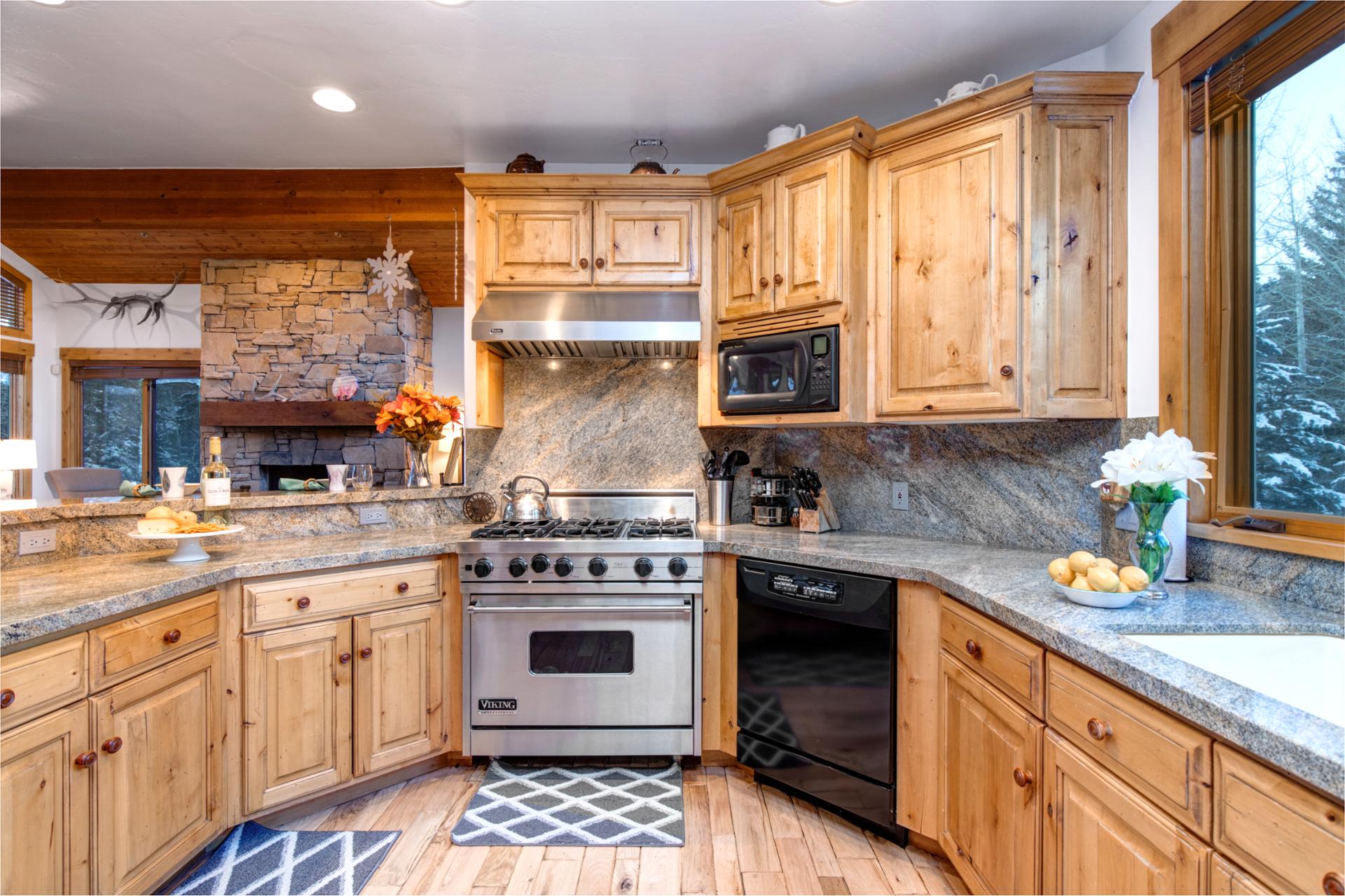 Cook with ease in the fully equipped kitchen featuring granite counters, gas range, and warm wood cabinetry, with open sightlines to the living area and fireplace.