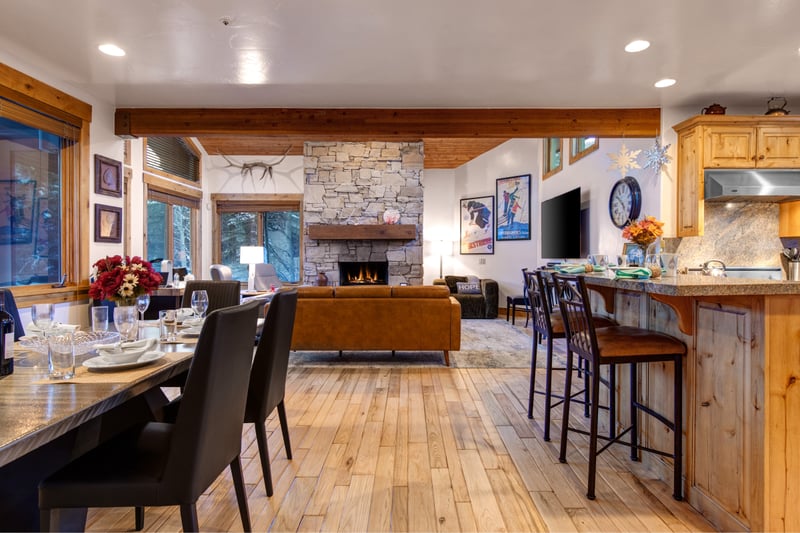 Open-concept living, dining, and kitchen with vaulted wood-beam ceilings, a stone fireplace, and leather sofa seating