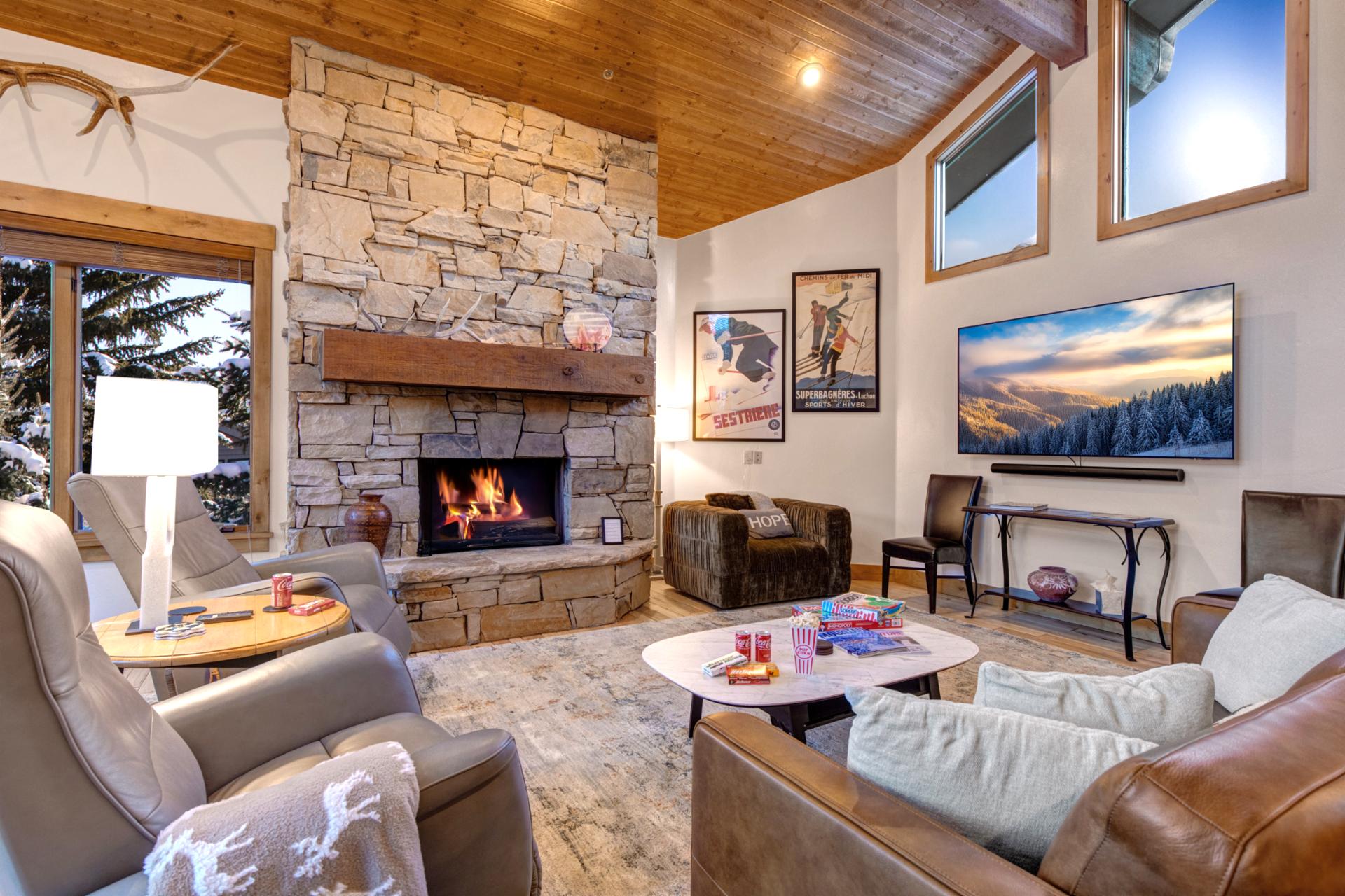Gather in the living area with a stone fireplace, mounted TV, and plush seating beneath soaring wood cathedral ceilings for cozy evenings together.