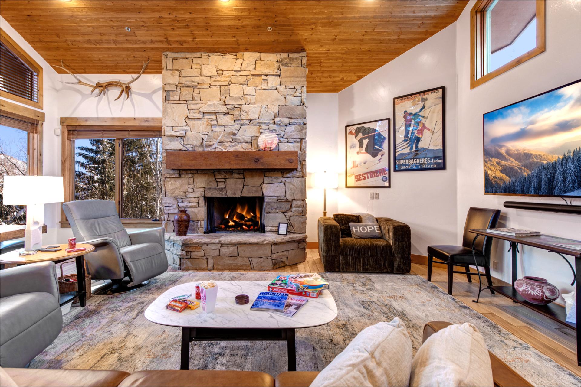 Enjoy cozy evenings by the stone fireplace in this Deer Valley living room, with leather seating, large Smart TV, and mountain views through the windows inviting you to relax after skiing.
