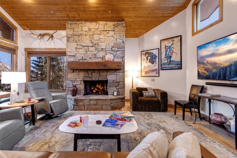 Enjoy cozy evenings by the stone gas fireplace in this Deer Valley living room, with leather seating, large Smart TV, and mountain views through the windows inviting you to relax after skiing.